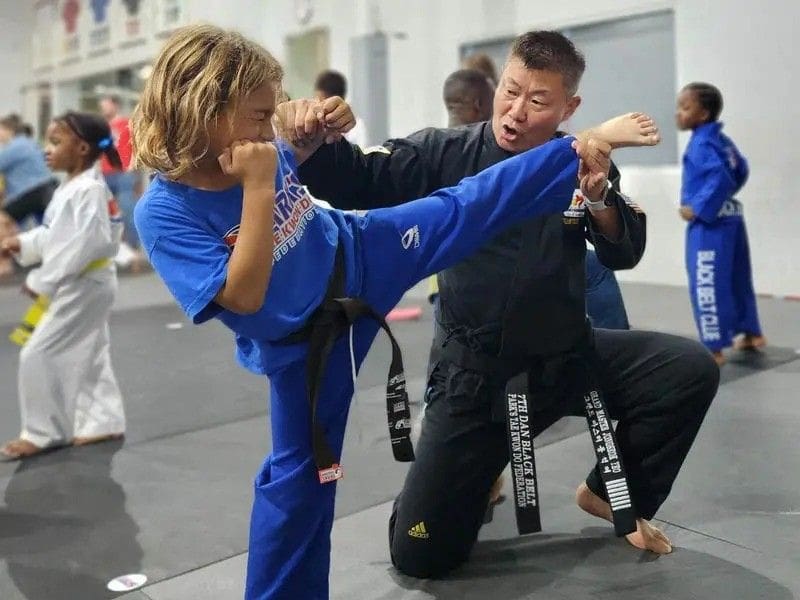 Instructor guiding a child through proper kicking form in a hands-on martial arts class.