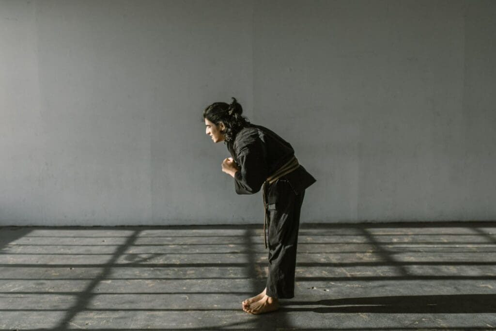 Martial arts practitioner bowing with hands clasped in front of a white wall how to improve balance in taekwondo
