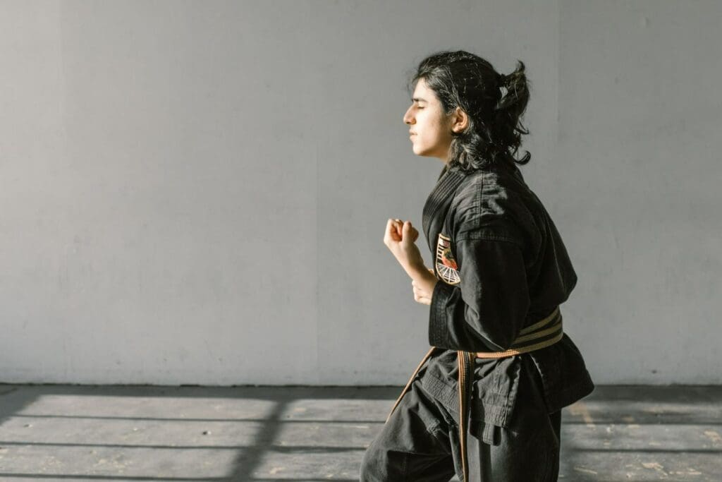 Martial arts practitioner holding a low fist guard while facing forward against a plain wall how to improve balance in taekwondo